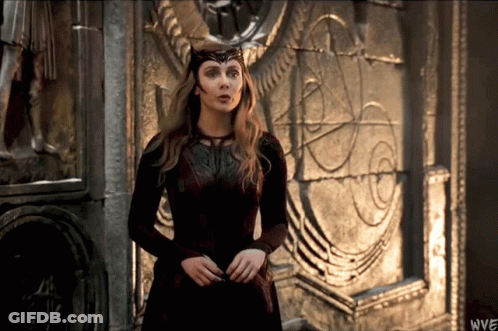 A Woman In A Red Dress Is Standing In Front Of A Stone Wall With The Letters Wwe On The Bottom Right GIF