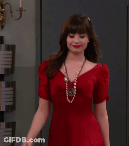 A Woman In A Red Dress Is Standing In Front Of A Wall GIF