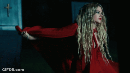 A Woman In A Red Dress Is Standing In Front Of A Wall With A Cross On It GIF