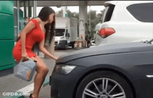 A Woman In A Red Dress Is Standing Next To A Car Holding A Gallon Of Oil GIF