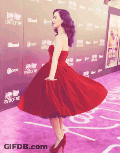 A Woman In A Red Dress Is Standing On A Purple Carpet With Pepsi And Billboard Signs Behind Her GIF
