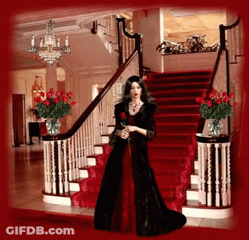 A Woman In A Red Dress Is Standing On A Set Of Stairs GIF