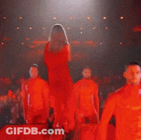 A Woman In A Red Dress Is Standing On A Stage GIF