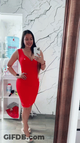 A Woman In A Red Dress Is Taking A Picture Of Herself In Front Of A Mirror GIF