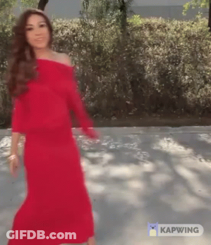 A Woman In A Red Dress Is Walking Down A Road . GIF