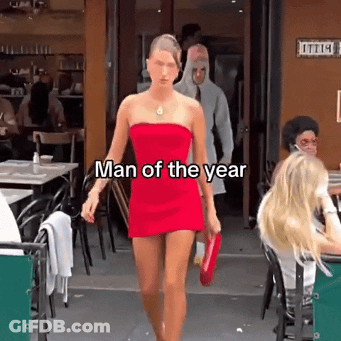 A Woman In A Red Dress Is Walking In Front Of A Restaurant With The Words Man Of The Year On The Bottom GIF