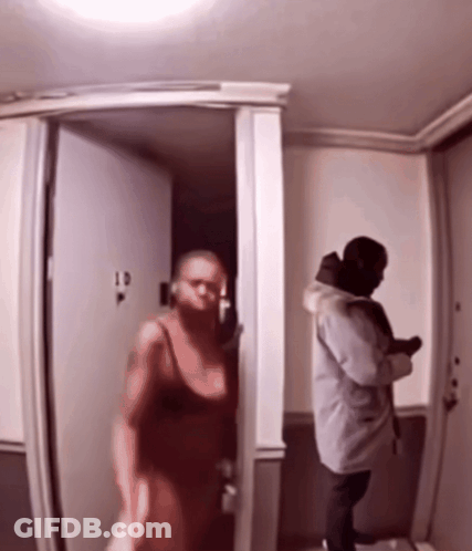 A Woman In A Red Dress Is Walking Into A Room With A Man In A Grey Coat GIF