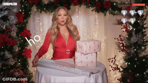 A Woman In A Red Dress Is Wrapping Presents In Front Of A Christmas Tree And A Sign That Says Cosmopolitan GIF