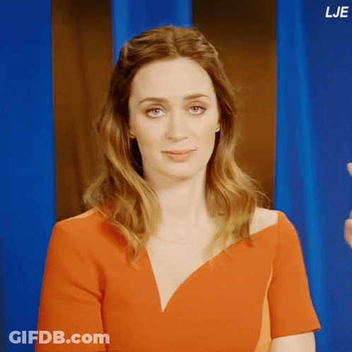 A Woman In A Red Dress Stands In Front Of A Blue Curtain With The Letters Lje On The Bottom Right GIF