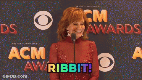 A Woman In A Red Dress Stands In Front Of A Microphone With The Words Acm Awards Behind Her GIF