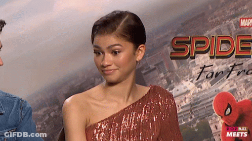 A Woman In A Red Dress Stands In Front Of A Poster That Says Spider-Man Far From Home GIF