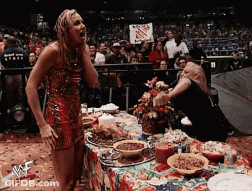 A Woman In A Red Dress Stands In Front Of A Table With A Wwe Logo GIF