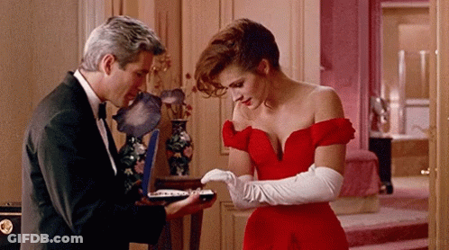 A Woman In A Red Dress Stands Next To A Man In A Black Suit GIF