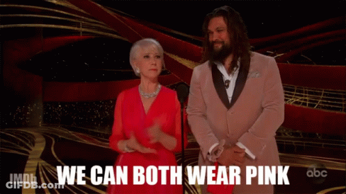 A Woman In A Red Dress Stands Next To A Man In A Pink Suit With The Words We Can Both Wear Pink Behind Them GIF