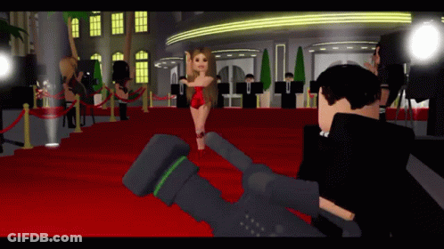 A Woman In A Red Dress Stands On A Red Carpet In Front Of A Camera GIF