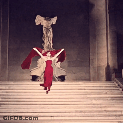 Woman In Red Dress On Stairs In Front Of Statue GIF