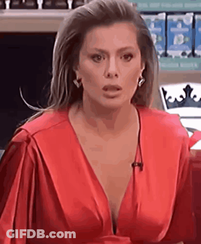 A Woman In A Red Dress With A Plunging Neckline Is Talking On A Microphone . GIF