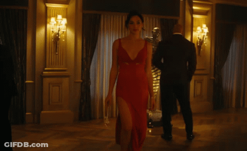 A Woman In A Red Dress With A Plunging Neckline Is Walking In A Room GIF