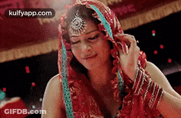 A Woman In A Red Dress With A Veil On Her Head Is Looking Down . GIF
