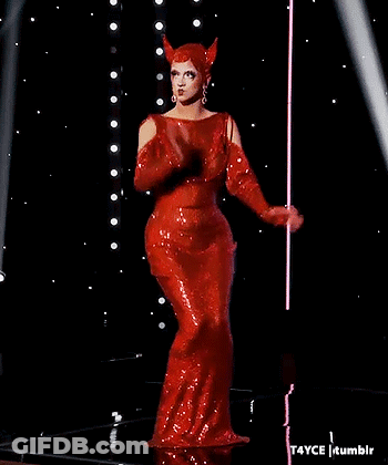 A Woman In A Red Dress With Horns On Her Head Is Standing On A Stage . GIF