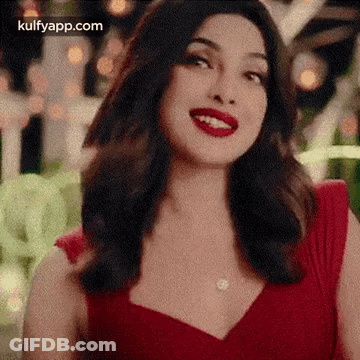 A Woman In A Red Dress With Red Lipstick Is Smiling . GIF