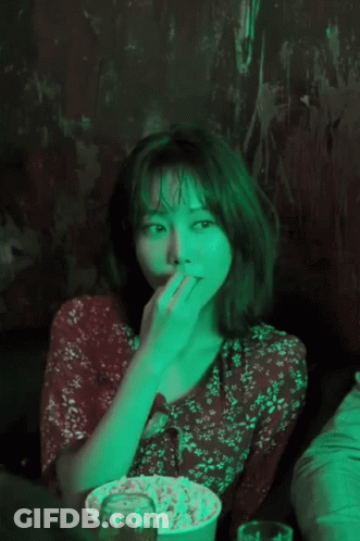 A Woman In A Red Floral Dress Is Eating Popcorn In A Dark Room GIF