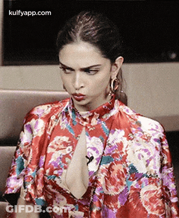 A Woman In A Red Floral Dress Is Sitting On A Couch . GIF
