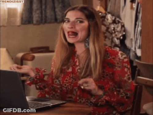 A Woman In A Red Floral Shirt Is Sitting At A Table With A Laptop . GIF