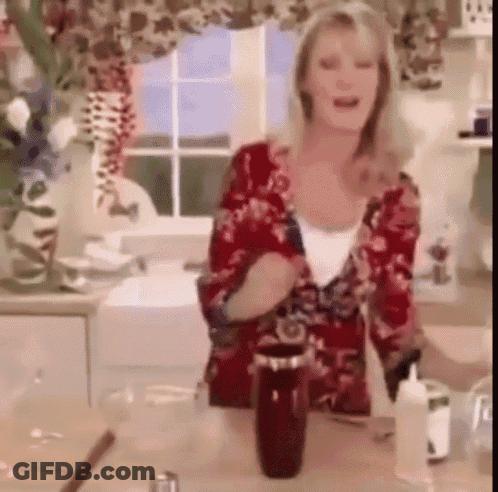 A Woman In A Red Floral Shirt Is Standing In A Kitchen Next To A Bottle GIF