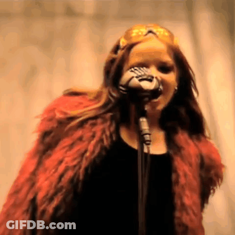 A Woman In A Red Fur Coat Singing Into A Microphone . GIF