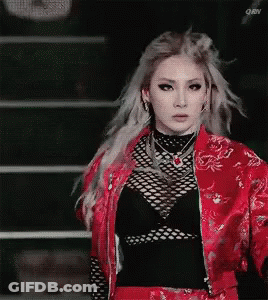 A Woman In A Red Jacket And Black Top Is Standing In Front Of A Staircase . GIF