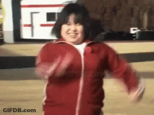 A Woman In A Red Jacket Is Dancing In Front Of A Bus . GIF