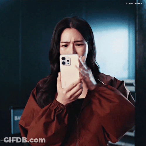 A Woman In A Red Jacket Is Looking At Her Phone And Making A Face GIF