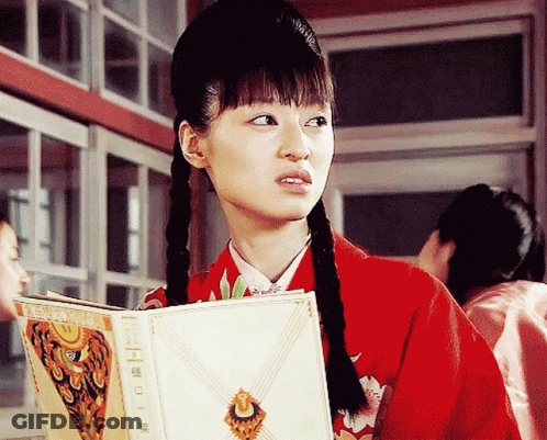 A Woman In A Red Jacket Is Reading A Book With Chinese Writing GIF