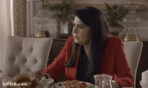 A Woman In A Red Jacket Is Sitting At A Table With A Plate Of Food GIF