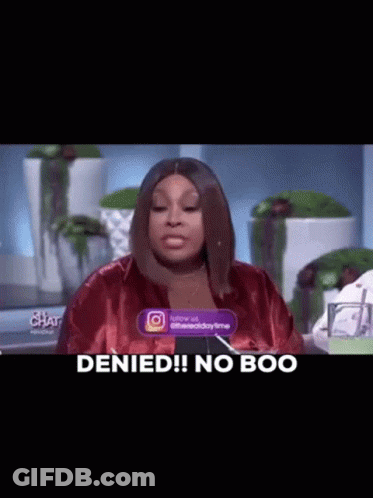 A Woman In A Red Jacket Is Sitting At A Table With A Sign That Says `` Denied ! No Boo '' . GIF