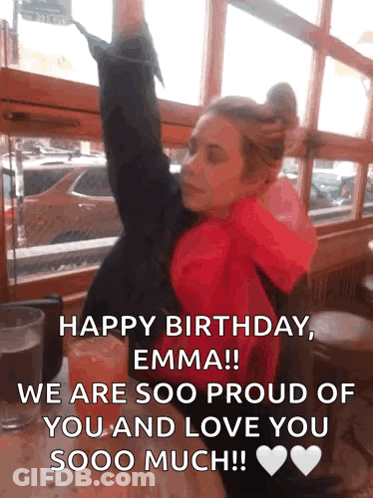 A Woman In A Red Jacket Is Sitting At A Table With Her Arms In The Air And A Birthday Message GIF