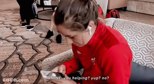 A Woman In A Red Jacket Is Sitting On A Couch Looking At Her Phone And Says " Janine You Helping " GIF
