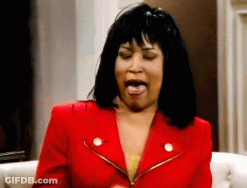 A Woman In A Red Jacket Is Sitting On A Couch With Her Mouth Open GIF