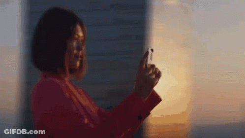 A Woman In A Red Jacket Is Taking A Picture Of The Sunset With Her Phone GIF