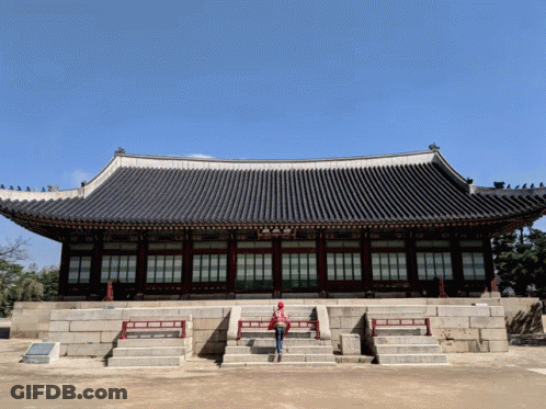 A Woman In A Red Jacket Stands In Front Of A Building GIF