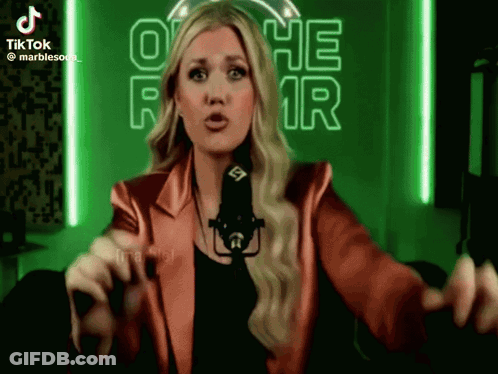 A Woman In A Red Jacket Stands In Front Of A Microphone In Front Of A Neon Sign That Says O He R GIF