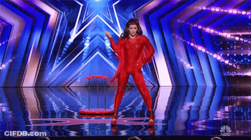 A Woman In A Red Jumpsuit Is Dancing On A Stage With A Star In The Background . GIF