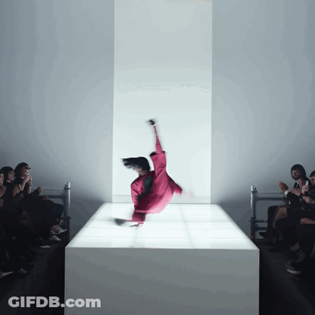 A Woman In A Red Jumpsuit Is Doing A Trick On A White Podium GIF