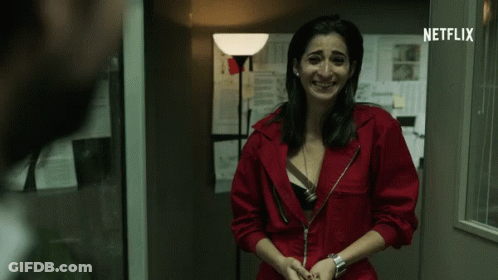 A Woman In A Red Jumpsuit Is Smiling In Front Of A Netflix Sign GIF