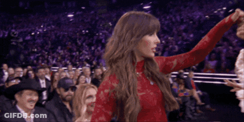 A Woman In A Red Lace Top Stands In Front Of A Crowd GIF