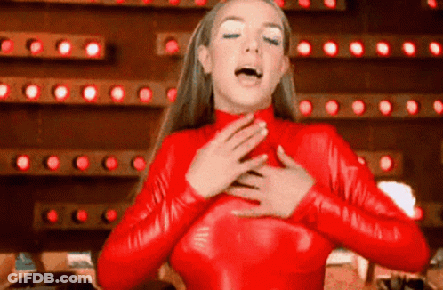 A Woman In A Red Latex Outfit Is Singing Into Her Mouth . GIF