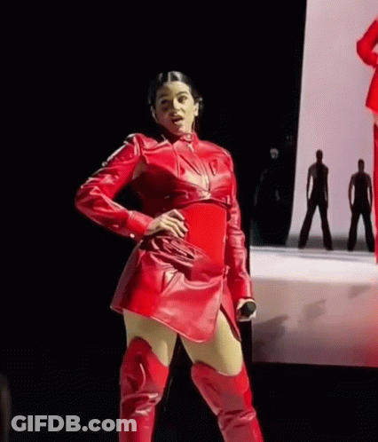A Woman In A Red Leather Dress And Red Boots Is Standing On A Stage . GIF