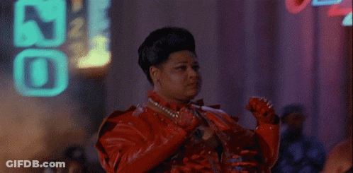 A Woman In A Red Leather Jacket Is Standing In Front Of A Neon Sign That Says ' J ' On It GIF