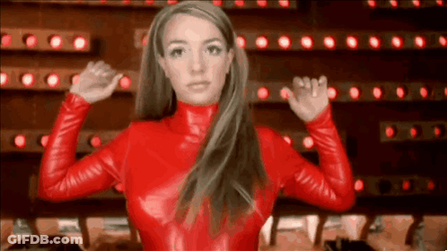 A Woman In A Red Leather Outfit Is Standing In Front Of A Wall Of Lights And Flexing Her Muscles . GIF